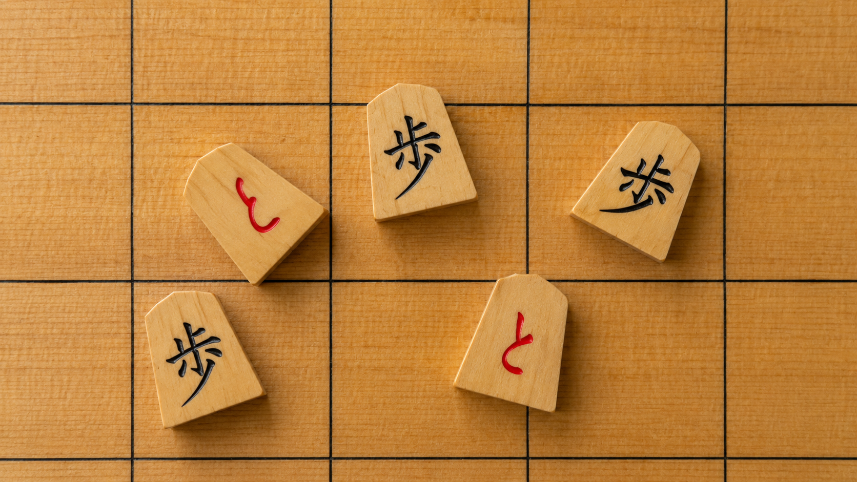 Five shogi pawns scattered on a wooden board after a furigoma toss, showing three fu and two tokin facing up