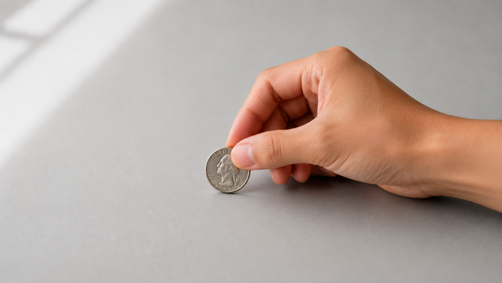 A hand picking up a silver coin from a flat surface